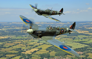 two spitfires flying in a blue sky over green fields